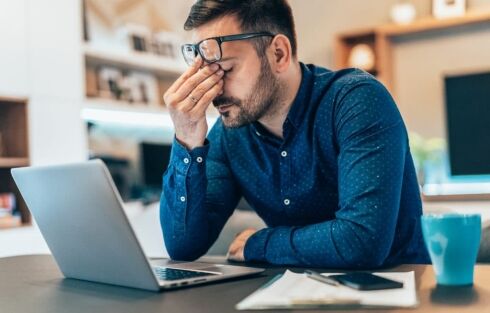 Tired and fatigued young businessman with nutrient deficiency working at home using lap top