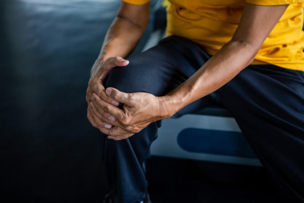 Person gripping knee in pain as result of osteoarthritis