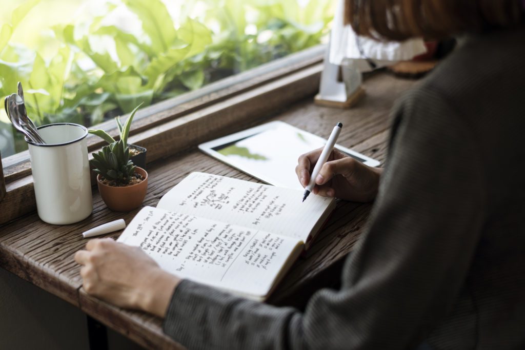 Woman sitting at wooden table writing in good habits journal