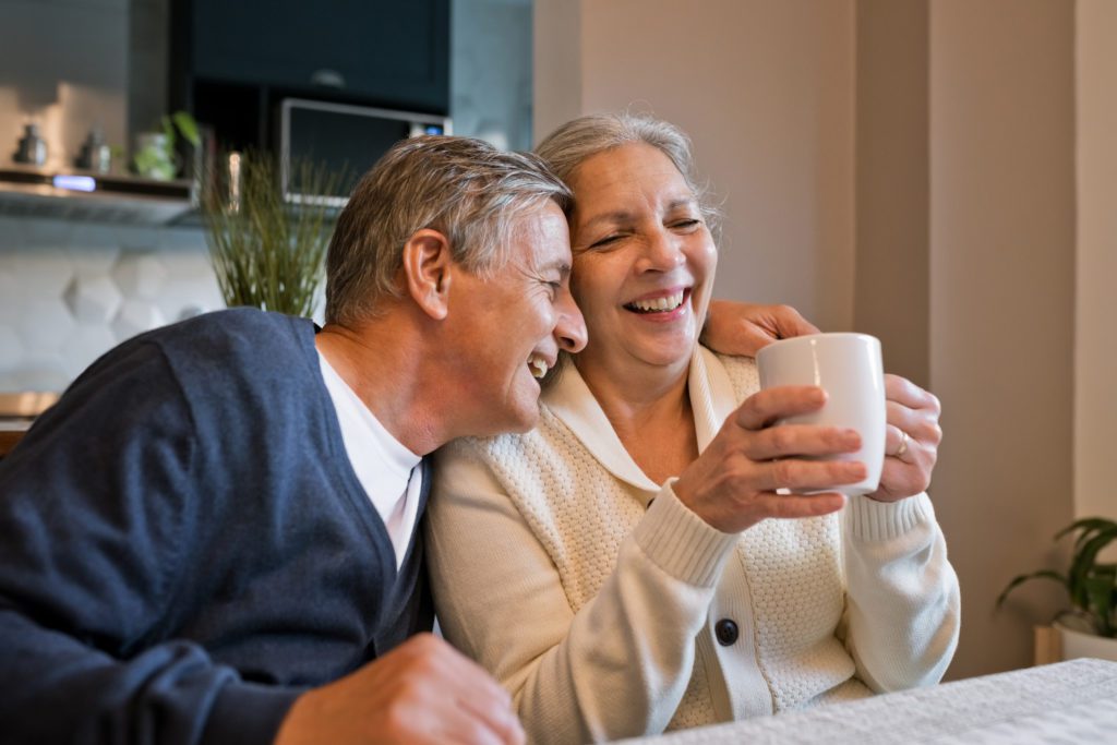 Cheerful senior woman and man sitting having coffee at home having recovered from a stroke. 