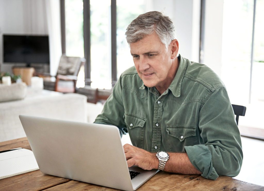 Man sitting at his laptop at home doing an online video consult with a pharmacist 