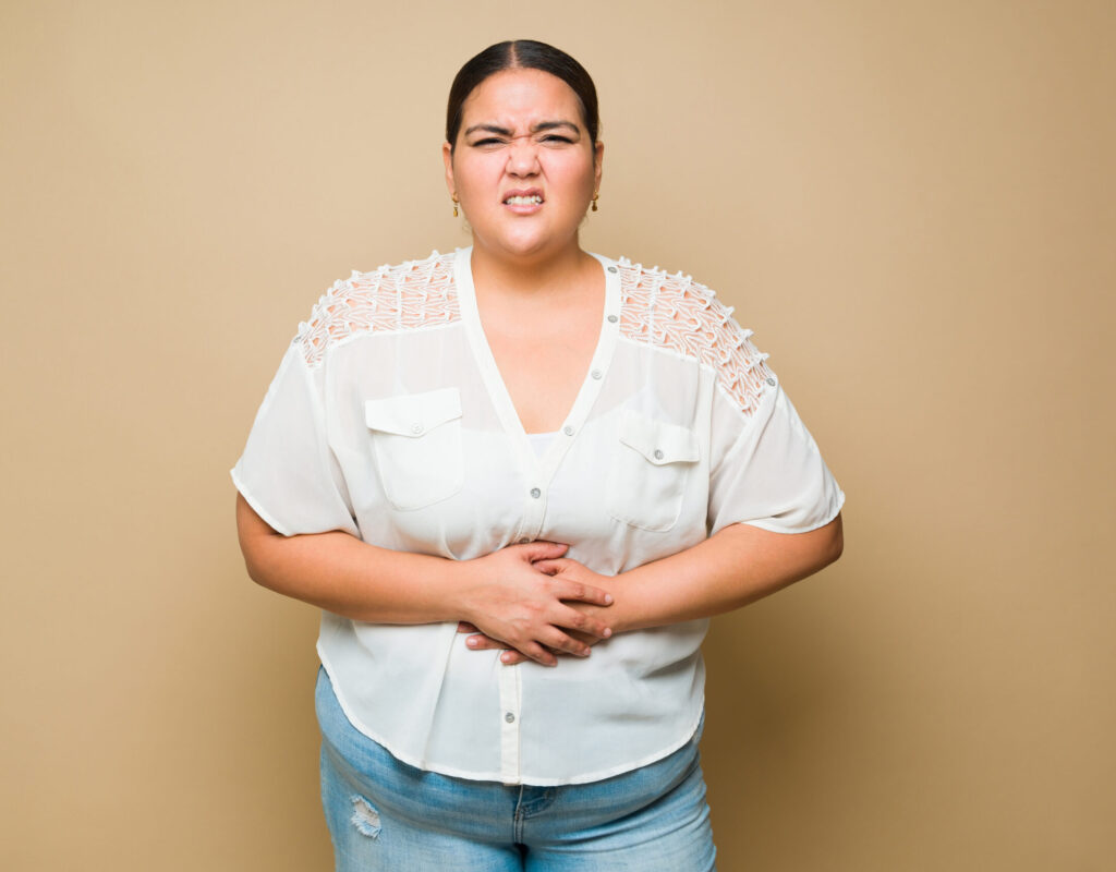 Sick overweight woman touching her abdomen and feeling pain because of a stomachache or cramps