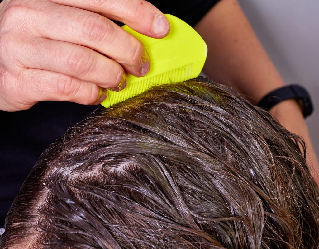 person checking wet hair for lice, with a yellow lice comb