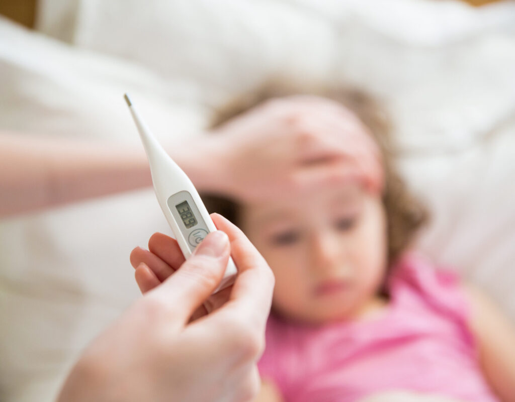 Close-up thermometer. Mother measuring temperature of her ill kid. Sick child with high fever laying in bed and mother holding thermometer. Hand on forehead.